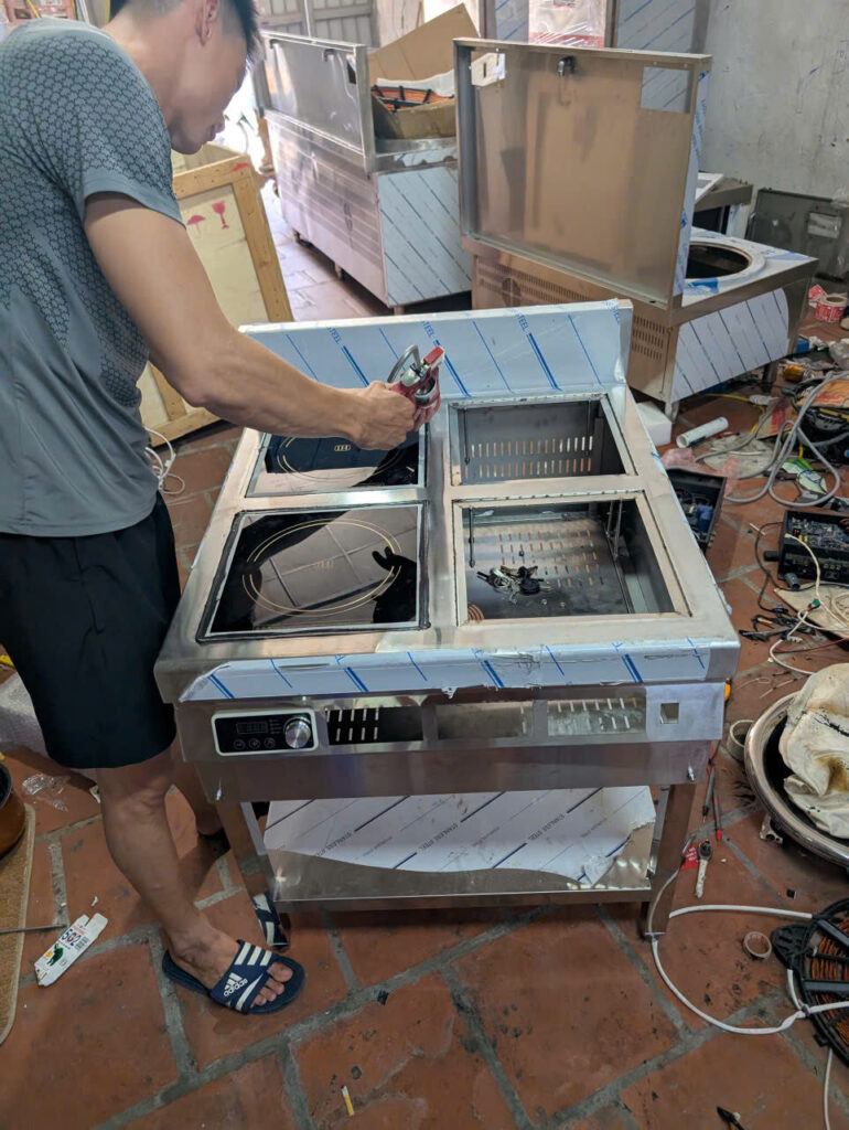 Kỹ thuật viên thực hiện kiểm tra an toàn, rò rỉ điện nước cho các thiết bị bếp từ công nghiệp sau lắp đặt.